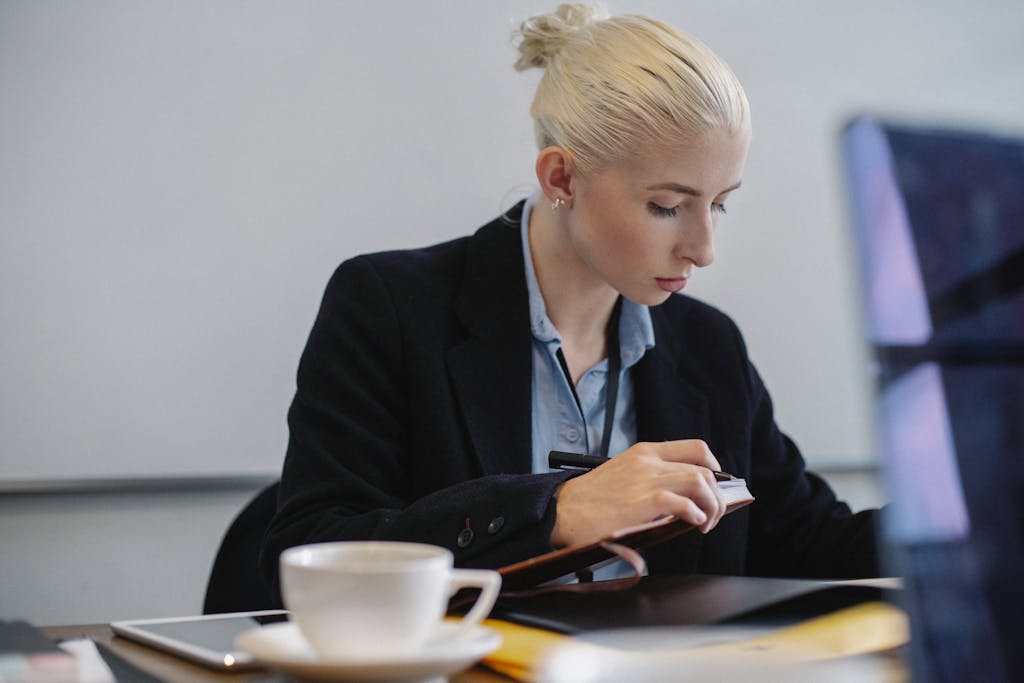 young businesswoman in formal outfit checking documents at table with cup in office young businesswoman in formal outfit checking documents at table with cup in office